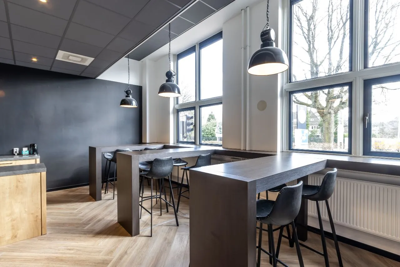 Moderne zithoek met hoge tafels en barkrukken bij grote ramen aan de Lage Naarderweg.